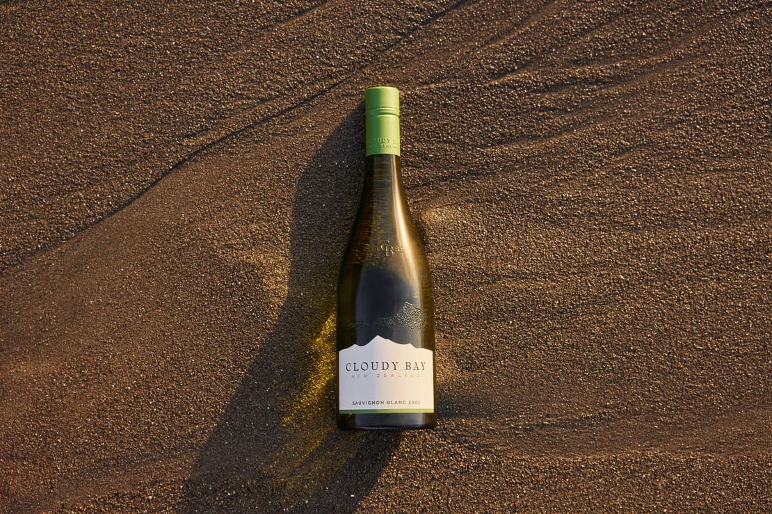 Cloudy Bay's new bottle design featuring the silhouette of the Richmond Ranges. The bottle is photographed laid down flat on a sandy beach
