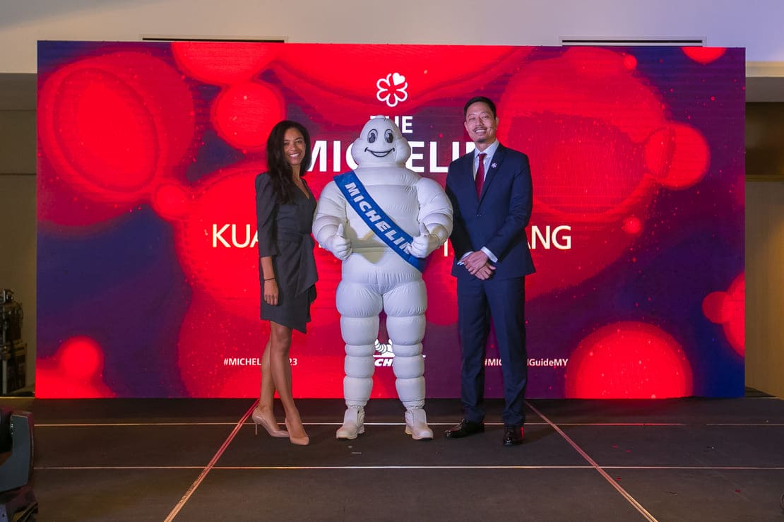 MICHELIN Experiences and Director of Communications Elisabeth Boucher-Anselin, the MICHELIN Man, and Managing Director of MICHELIN Malaysia, Singapore, and Brunei Prichapakorn Dangrojana stand in front of the MICHELIN Guide photowall at the announcement press conference.